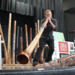 Didgeridoo Down Under plays a didgeridoo on a stage with many items