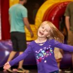 young girl holds arms out smiling and holds balloon animal