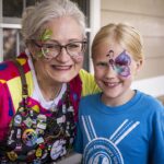 face painter poses with smiling girl who just had butter fly face paint down