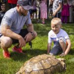 adult and boy crouch to look at turtle in grass
