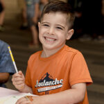 Young boy holds pencil and smiles at camera