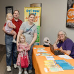 family poses with a librarian at "Get Your Library Card" station