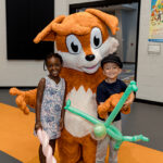 two young children hold their balloon art and pose with Booker the Fox mascot