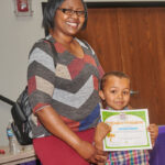woman poses with young boy who holds up his Imagination Graduation diploma