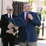 Man speaks into microphone, Karl stands in background