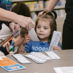 Young girl picks up color-your-own bookmarks