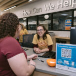 Head of Circulation Emilia standing behind the information desk smiling at a patron