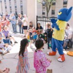 Children gather around Pete the Cat mascot on patio