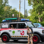 Teen dressed up as a ghostbuster poses in front of ghostbuster jeep