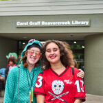 two teen girls smile and pose in front of entrance