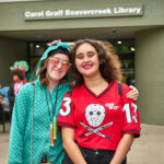 two teen girls smile and pose in front of entrance