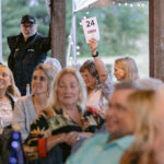 woman toward back of venue raising hand to bid on auction item