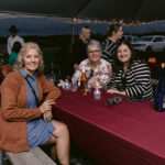 three women sitting at a picnic table smiling and enjoying wine