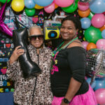two attendees posing in front of photo station holding boombox and phone props